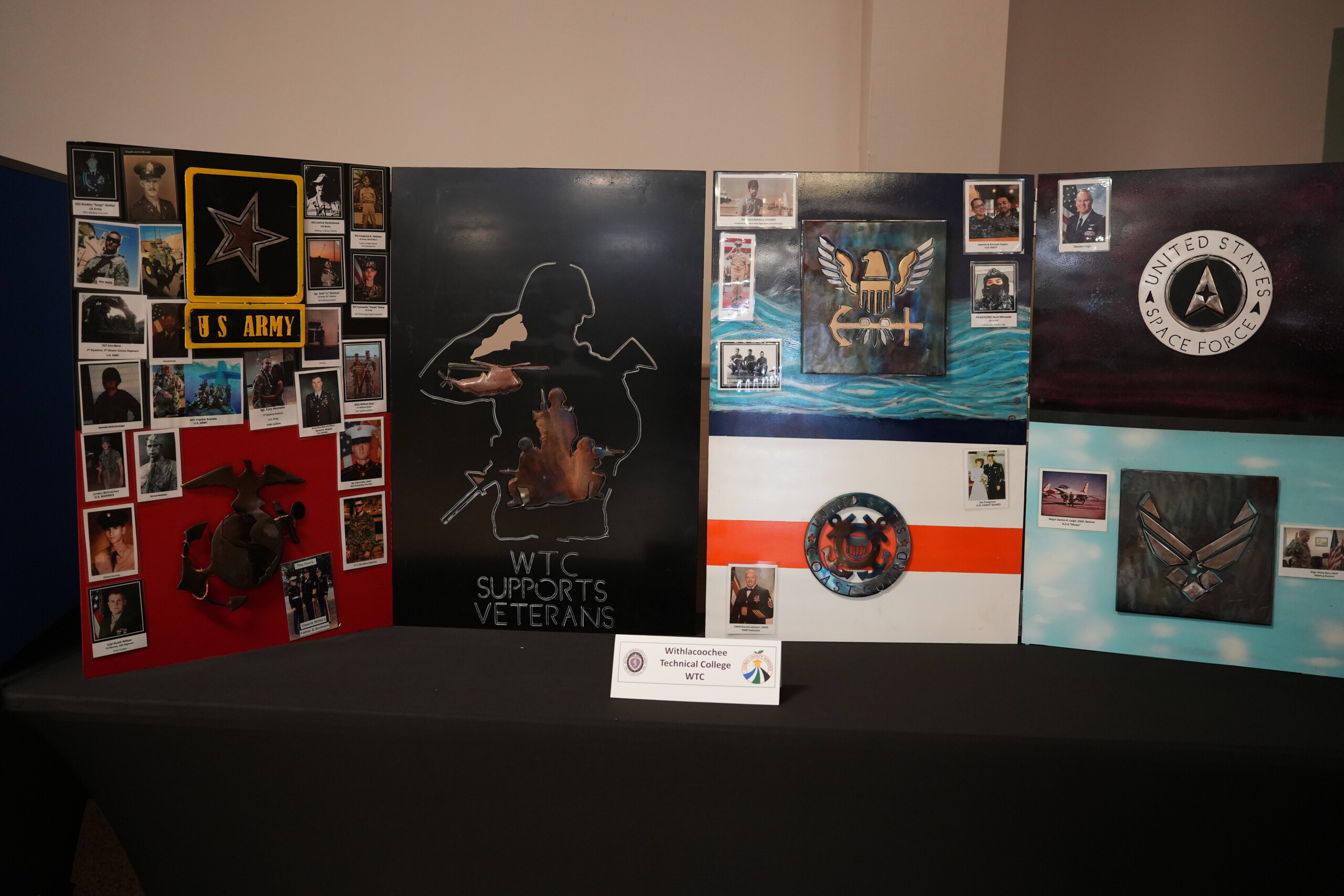 A multi-panel display on a table features military branch logos, photos, and a sign reading 'WTC SUPPORTS VETERANS'.